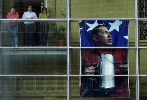 Funcionários da Assembleia venezuelana olham de terraço ao lado de pôster de Hugo Chávez (Foto: Juan Barreto/AFP)